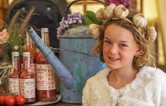 A girl wearing a garlic headband standing next to local produce at the Isle of Wight Garlic Festival, what's on, event