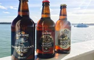 Three bottles of beer on ledge overlooking solent with ferry in background, Isle of Wight, Local Produce, Island Brewery, let's buy local