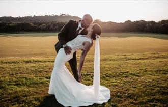 Couple kissing outside within the grounds of Newclose County Cricket Ground with the sun setting, weddings on the Isle of Wight, celebration, family,