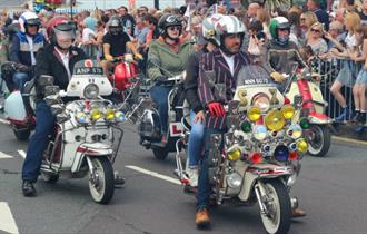 Isle of Wight Scooter Rally, image of Scooter Riders riding along road with onlookers applauding