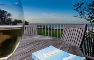 Glass of wine and book on the outside dining tables with sea views at Beach Cottage, Fort Victoria Cottages, Yarmouth, Isle of Wight, self catering