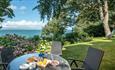 Outside table and chairs surrounded by green grass, trees and plants with a seaview - self-catering, Isle of Wight, HB Holiday Lettings