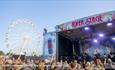 Crowds watching a band on the River stage with the wheel ride in the background at the Isle of Wight Festival, music event, what's on