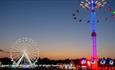 Big wheel ride and the high swing ride with the sun set in the background at the Isle of Wight Festival, music event, what's on