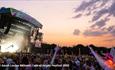 Crowds watching a band on the main stage in the evening with the sun set in the background at the Isle of Wight Festival, music event, what's on