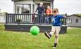 Boy playing with ball on the grass in front of the holiday home at St Helens Holiday Resort, Isle of Wight, Holiday Park