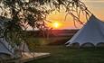 Outside view of bell tents at Warren Hill Camp with sunset in the background, glamping, accommodation, camping, Isle of Wight, family friendly, couple