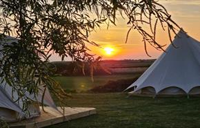 Outside view of bell tents at Warren Hill Camp with sunset in the background, glamping, accommodation, camping, Isle of Wight, family friendly, couple