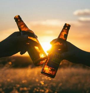 Two people clunking two bottles of beer together with a sunset behind, Beer, music and poetry festival at Waverley Park Holiday Centre, Isle of Wight,