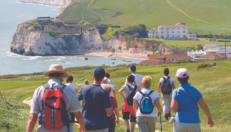 Group of people walking towards Freshwater Bay with Freshwater Bay House in the background, walking holiday, Isle of Wight