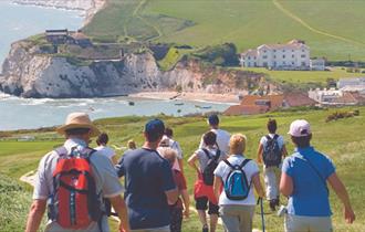 Group of people walking towards Freshwater Bay with Freshwater Bay House in the background, walking holiday, Isle of Wight