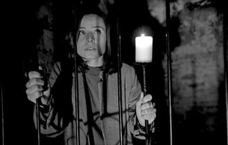 Girl standing behind bars with candle, The Lost Crypt Escape Room at Aspire Ryde, Isle of Wight, Things to Do