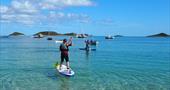 Stand up paddleboarders having fun off Par Beach, it's a calm sunny day with clear blue water. 
