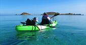 A mother and son kayaking on still crystal clear water on a calm sunny day with the Eastern Isles in the background.
