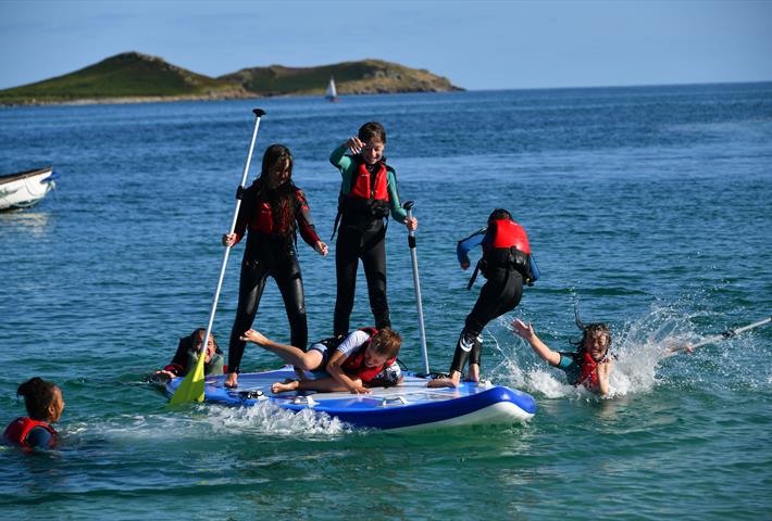 Children playing on a four person paddle board having fun falling into the water.
