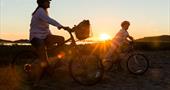 Adult and child cycling beside the beach at sunset