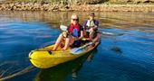 A couple and their dog are in a double kayak on calm seas out by the Eastern Islands.
