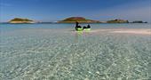 Two boys kayaking on Ganilly sandbar, the sea is crystal clear and the Eastern Isles are in the distance. 
