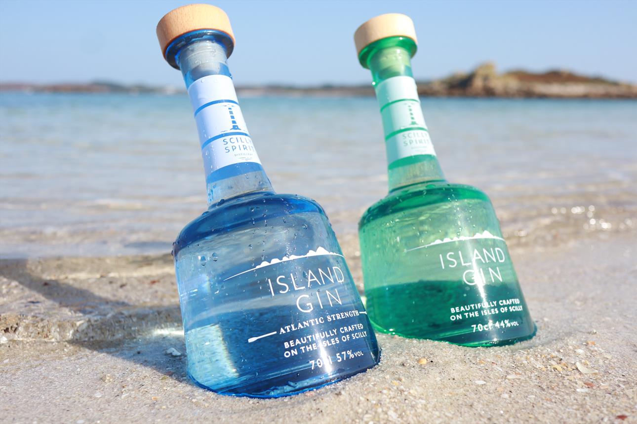 Picture of an aqua bottle of Island Gin and an azure blue bottle Atlantic Strength in the sand.