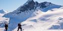 BIlete av to skiløparar på topptur, strålande vær og vakkert fjell i bakgrunnen. Aktiv i Lom.