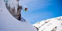 Picture of ski hiker skiing downwards and jumping of a berg formation in the mountainside.