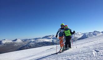 Bilde fra bakken med to skiløpere. strålende sol, blå himmel. Galdhøpiggen sommerskisenter, Galdhøpiggen summer skiing center, juvass