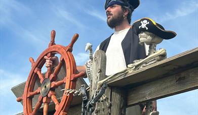 A man dressed as a pirate with a ship's wheel, and a skull with a pirate's hat on it