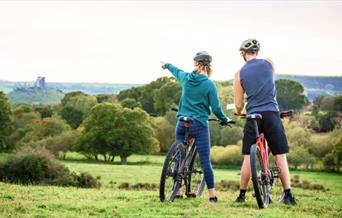 Image of a male and female on a bike in a field with trees around pointing at the landscape