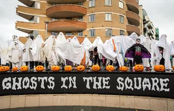 Picture showing a load of people dressed up a ghosts with lots of pumpkins above a sign saying Ghosts in the Square