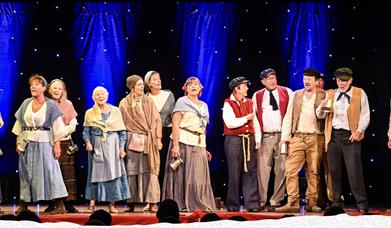 Picture of a group of people singing on stage dressed in sea shanty clothes