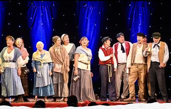 Picture of a group of people singing on stage dressed in sea shanty clothes