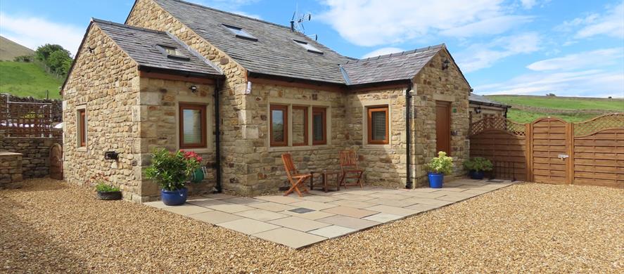 The sun shines on the cottage, surrounded by green hills.