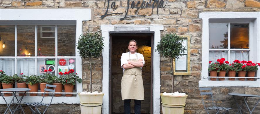 The chef stands proudly in the doorway of the restaurant, arms crossed.