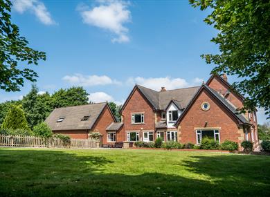 Outside view of the farmhouse, set in the countryside, on a bright sunny day.