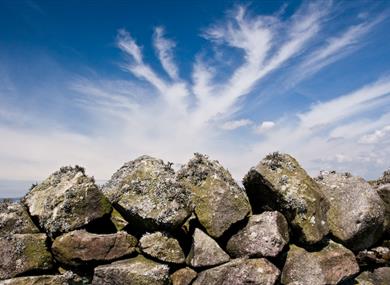 Dry stone wall with blue sky and clouds.