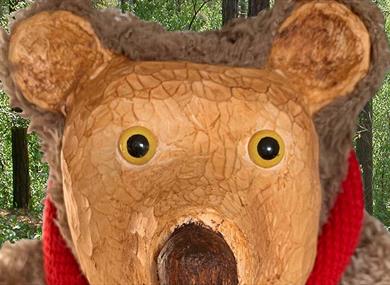 A brown bear stands in the woods, wearing a red scarf.