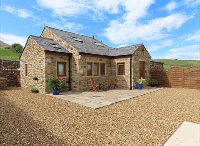 The sun shines on the cottage, surrounded by green hills.