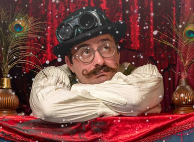The professor sits in a bowler hat, arms crossed in front of a red velvet curtain.  Snow is falling on him.