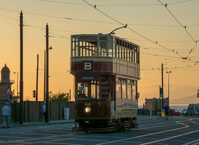 A heritage tram rides through Blackpool at sunset.