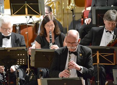 Various musicians play, sat behind the stands holding their sheet music.