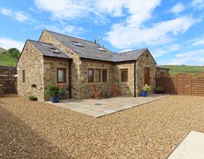 The sun shines on the cottage, surrounded by green hills.