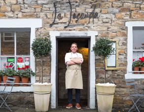 The chef stands proudly in the doorway of the restaurant, arms crossed.