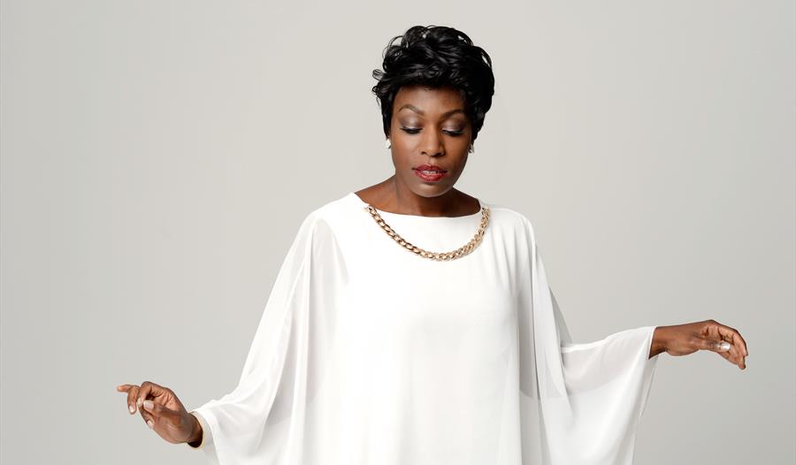 A simple photograph of the performer in all white dress and gold necklace.