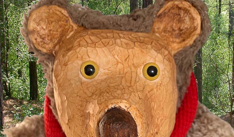 A brown bear stands in the woods, wearing a red scarf.