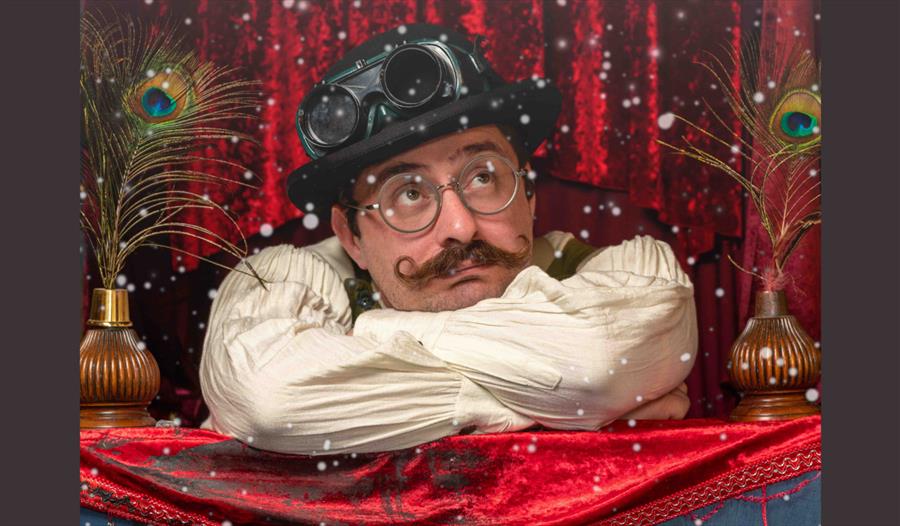 The professor sits in a bowler hat, arms crossed in front of a red velvet curtain.  Snow is falling on him.