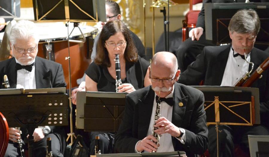 Various musicians play, sat behind the stands holding their sheet music.