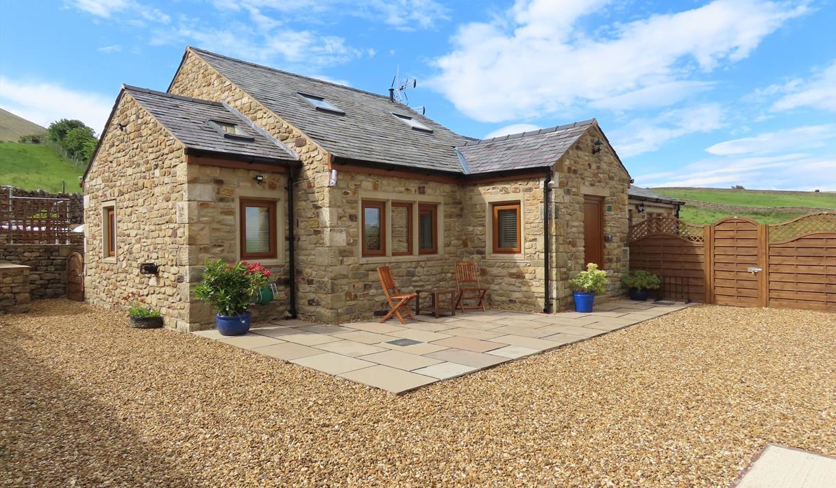 The sun shines on the cottage, surrounded by green hills.