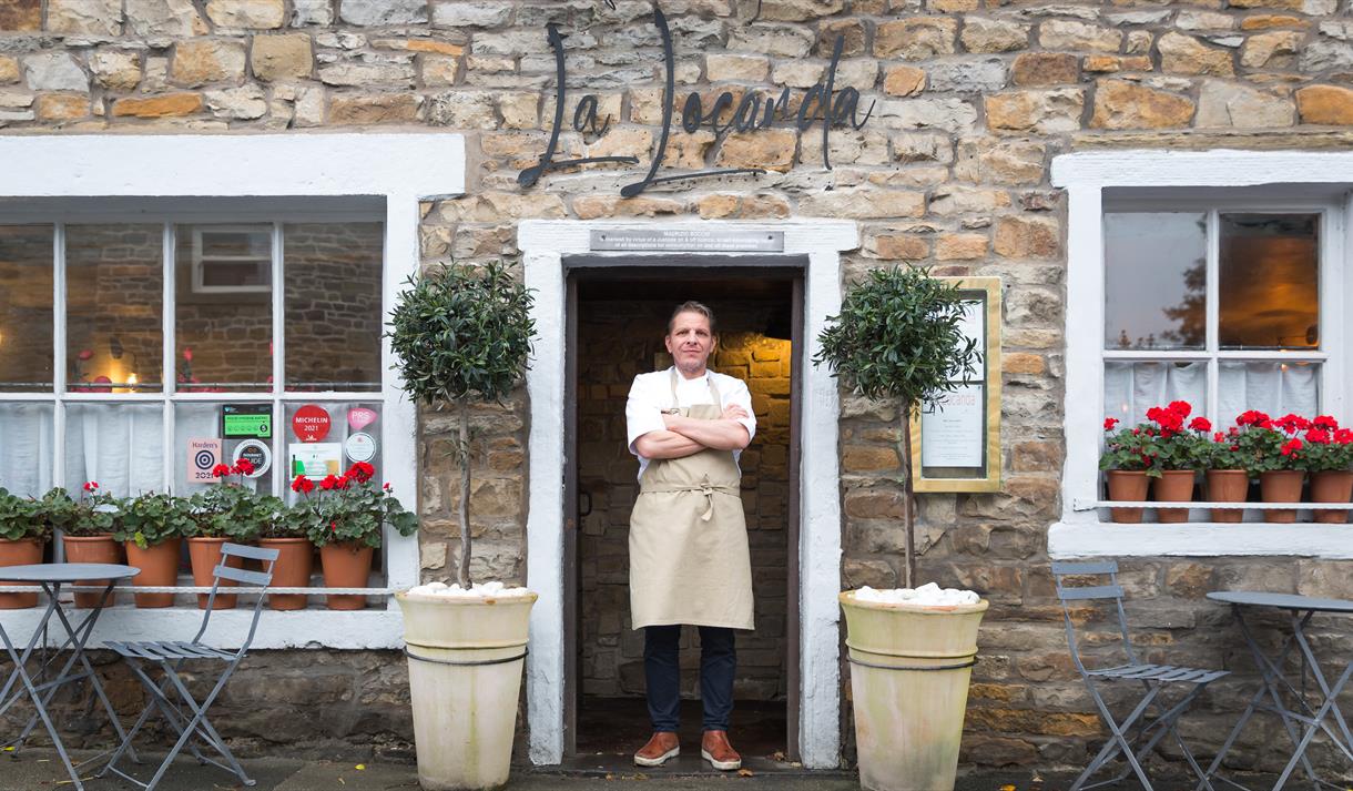 The chef stands proudly in the doorway of the restaurant, arms crossed.