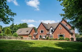 Outside view of the farmhouse, set in the countryside, on a bright sunny day.