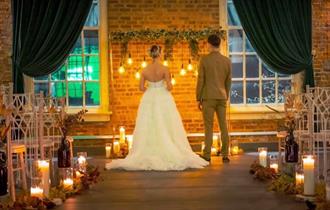 A couple stand in the venue with candles and lights decorating.
